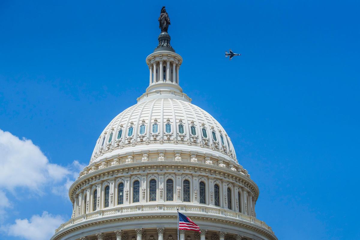 A jet flying over the US Capitol dome under a clear blue sky